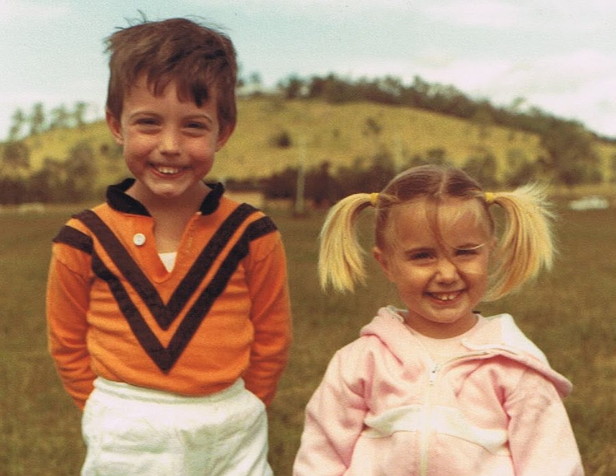 Jess and Josh as children, standing together on the grass.